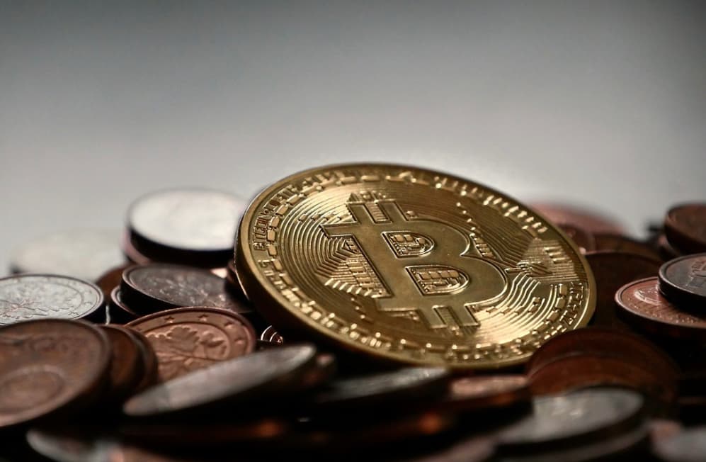 Close-up view of a golden Bitcoin coin amidst a pile of assorted world coins on a gray surface